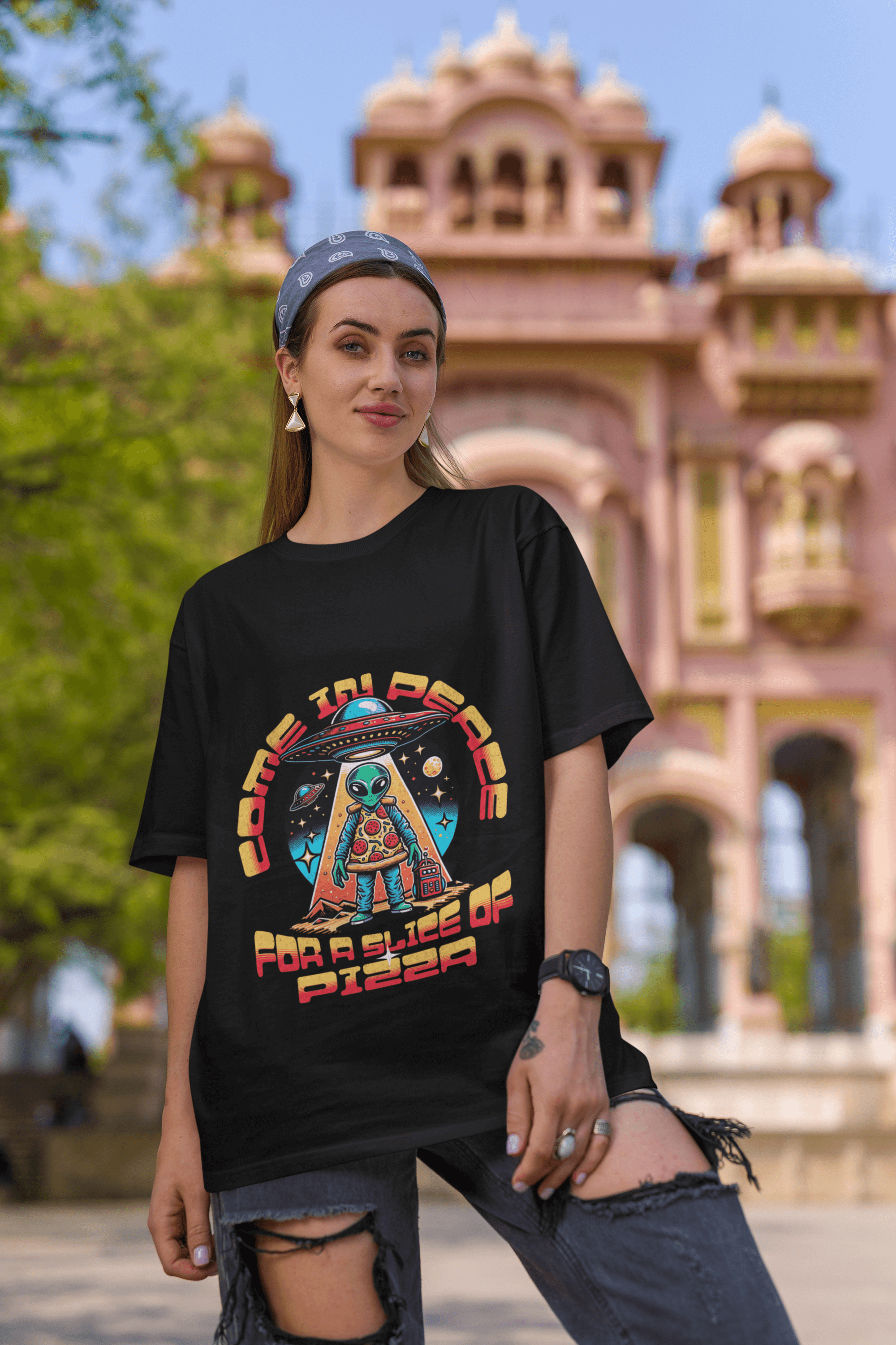 Unisex t-shirt nera boxy fit con grafica alieno pizza, 100% cotone, made in Italy, indossata da una ragazza con sfondo di edificio storico.